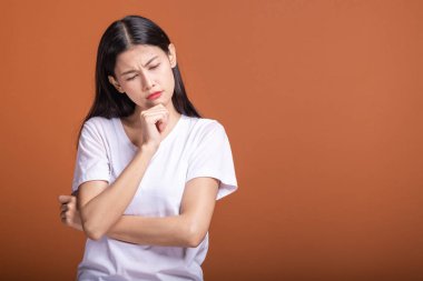 Turuncu arka plana düşünce kadın. Genç Asyalı hipster kadında ciddi düşünme poz ile beyaz t-shirt, çene parmağında. Genç kadın hipster kavramı.