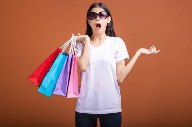 Alışveriş çantası turuncu arka planda izole tutan kadın. Genç Asyalı kadın beyaz t-shirt, şok ve sürpriz ruh hali. Alışveriş kavramı.