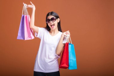 Alışveriş çantası turuncu arka planda izole tutan kadın. Beyaz t-shirt, mutlu ruh hali içinde Genç Asyalı kadın. Alışveriş kavramı.