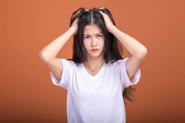 Turuncu arka plana düşünce kadın. Genç Asyalı hipster saç çekerek beyaz t-shirt ile karıştırmayın poz, kadında. Genç kadın hipster kavramı.