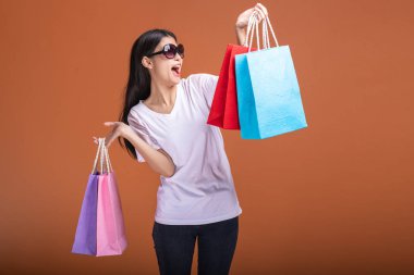 Alışveriş çantası turuncu arka planda izole tutan kadın. Beyaz t-shirt, mutlu ruh hali içinde Genç Asyalı kadın. Alışveriş kavramı.