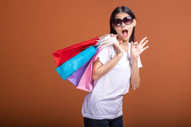 Alışveriş çantası turuncu arka planda izole tutan kadın. Beyaz t-shirt, şok ruh hali içinde Genç Asyalı kadın. Alışveriş kavramı.