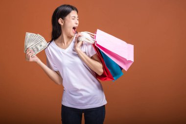 Alışveriş çantası ve turuncu arka planda izole para tutan kadın. Son derece heyecanlı ruh halinde beyaz t-shirt Genç Asyalı kadın. Tatil alışveriş kavramı.