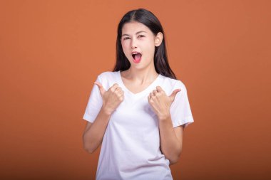 Turuncu arka plan üzerinde izole kadın kazanmak. Beyaz t-shirt ile kendine güvenen poz, iki el zam, kadında Genç Asyalı hipster yaşasın. Başarılı genç hipster kavramı.