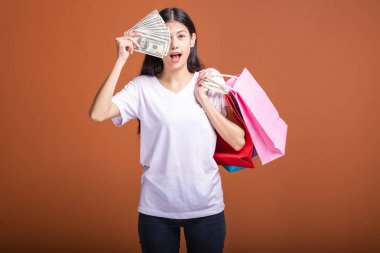 Alışveriş çantası ve turuncu arka planda izole para tutan kadın. Genç Asyalı kadın mutlu ruh hali içinde beyaz tişört içinde. Tatil alışveriş kavramı.