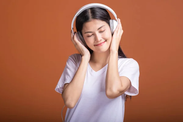 在橙色背景下使用耳机隔离的妇女 年轻的亚洲女人用头电话听音乐 放松心情愉快 时髦的生活方式概念 — 图库照片