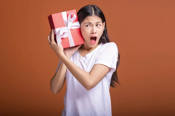 Young hipster girl got a gift. Asian woman in white t-shirt holding a red present gift box, extremely surprise mood. Holiday gift concept.