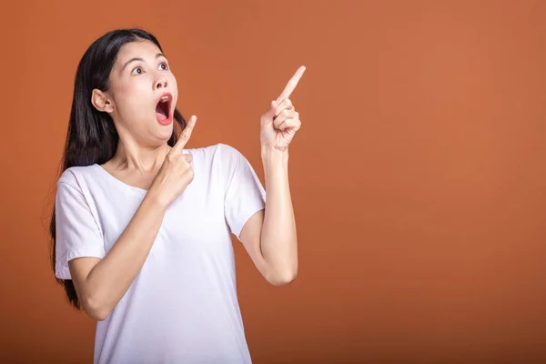 Surprise woman over orange background. Young Asian hipster woman in white t-shirt with very surprise pose, fingers pointing. Young woman hipster concept.