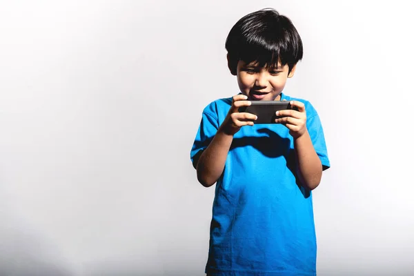 Young boy playing mobile game portrait in white background with hard light. Mixed race boy in blue shirt and jean. Happy win mood.
