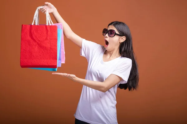 妇女拿着购物袋孤立的橙色背景 年轻的亚洲妇女穿着白色 T恤衫 震动心情 手包下 购物理念 — 图库照片