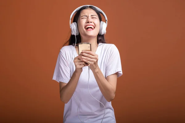 在橙色背景下 通过电话隔离的妇女听音乐 年轻的亚洲女人带着手机听音乐 心情很愉快 时髦的生活方式概念 — 图库照片
