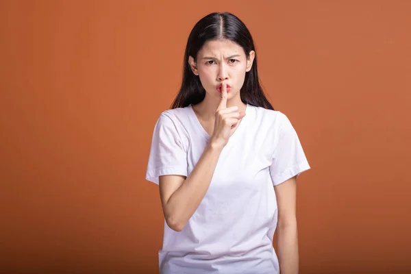 Woman doing secret hush pose. Asian woman in white t-shirt, isolated over orange background.