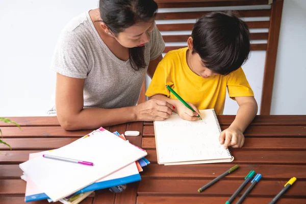 儿童作业 年轻的混血男孩在家的阳台上做作业 他的母亲教他 写作练习 集中心情 返回学校概念 — 图库照片