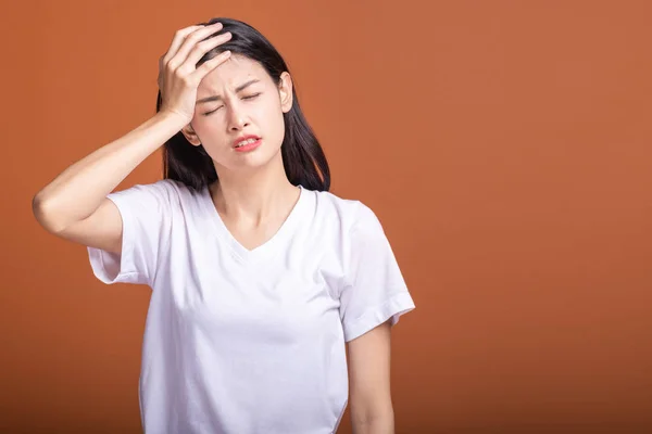 Thinking woman over orange background. Young Asian hipster woman in white t-shirt with headarch pose, hand on head. Young woman hipster concept.