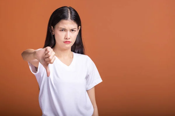 Upset woman isolated over orange background. Asian woman in white t-shirt doing thumb down pose, upset mood.