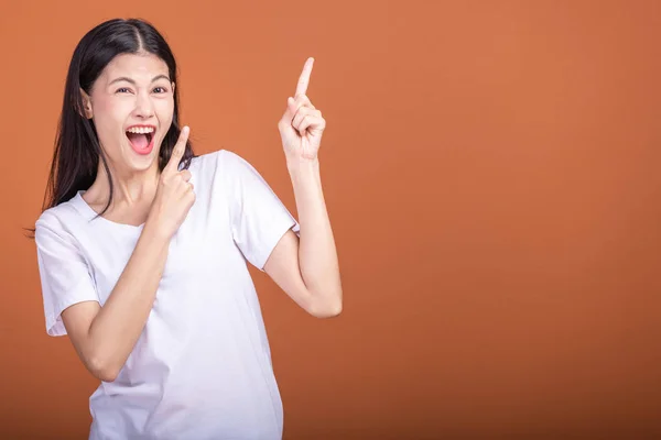 Surprise woman over orange background. Young Asian hipster woman in white t-shirt with surprise pose, fingers pointing. Young woman hipster concept.