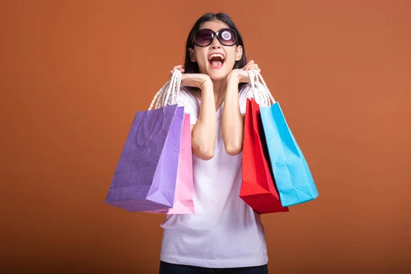 妇女拿着购物袋孤立的橙色背景 年轻的亚洲女人穿着白色 T恤衫 心情很愉快 包在脸上 购物理念 — 图库照片