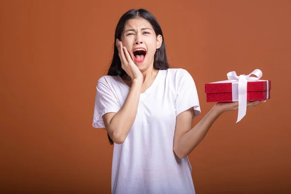 Young hipster girl got a gift. Asian woman in white t-shirt holding a red present gift box, extremely shock mood. Holiday gift concept.