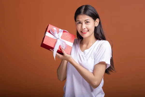 Young hipster girl got a gift. Asian woman in white t-shirt holding a red present gift box, happy smile mood. Holiday gift concept.