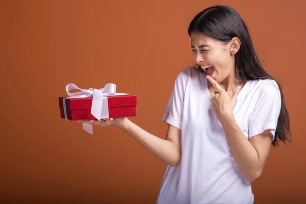 Young hipster girl got a gift. Asian woman in white t-shirt holding a red present gift box, shock mood. Holiday gift concept.