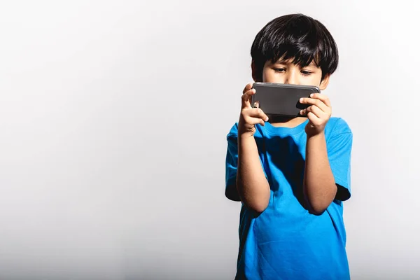 Young boy playing mobile game portrait in white background with hard light. Mixed race boy in blue shirt and jean. Focus mood.