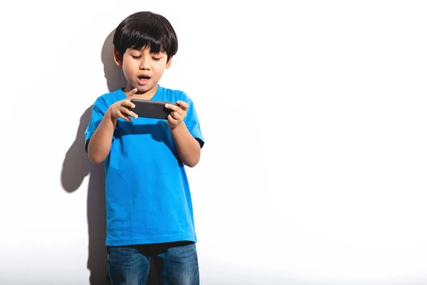 小男孩玩手机游戏肖像白色背景与硬光 穿着蓝色衬衣和琴的混血男孩 焦点情绪 — 图库照片