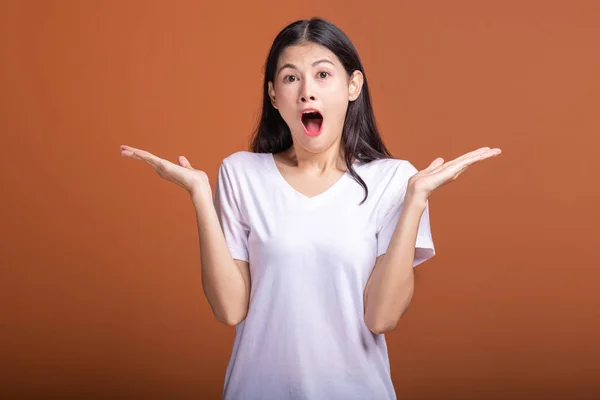 Surprise woman over orange background. Young Asian hipster woman in white t-shirt with surprise pose, open arms. Young woman hipster concept.