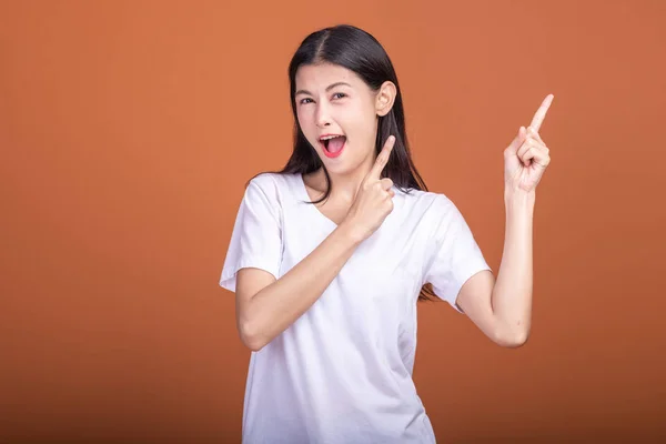 Surprise woman over orange background. Young Asian hipster woman in white t-shirt with surprise pose, fingers pointing. Young woman hipster concept.