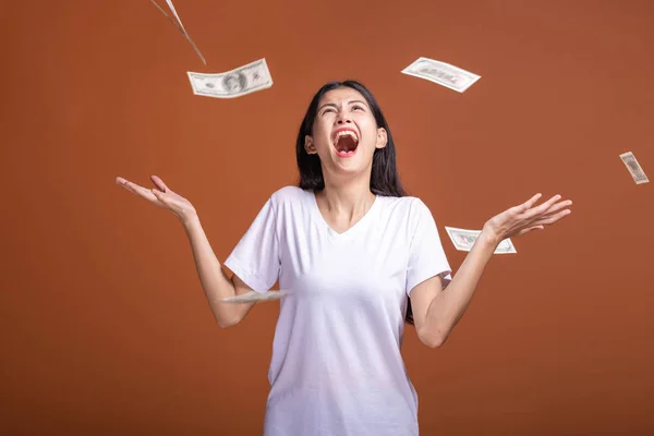 Money falling on woman isolated in orange background. Asian woman very happy as money falls on her. Rich young woman concept.
