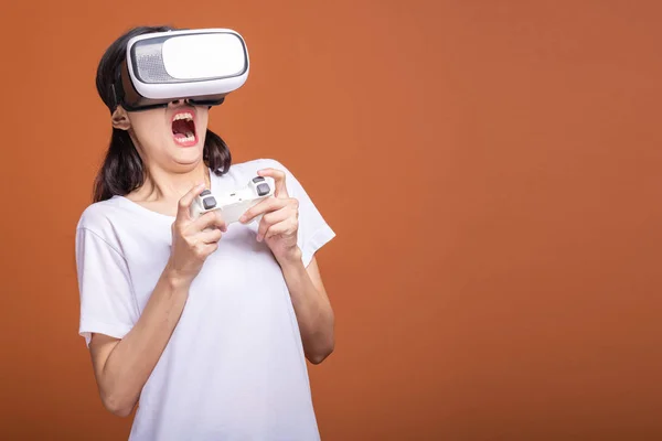 Woman wearing VR headset. Young Asian woman in white t-shirt with VR head gear, shocking scare pose. New entertainment concept.