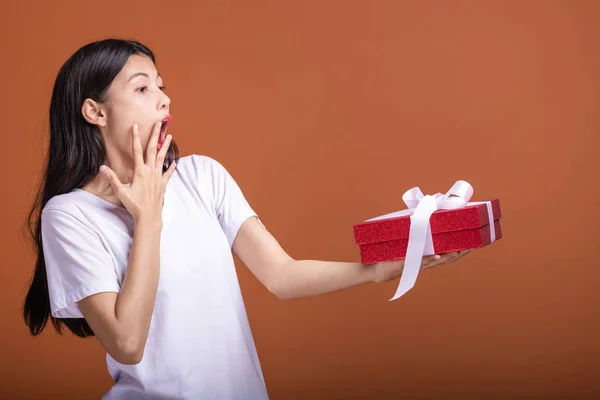 Young hipster girl got a gift. Asian woman in white t-shirt holding a red present gift box, extremely shock mood. Holiday gift concept.