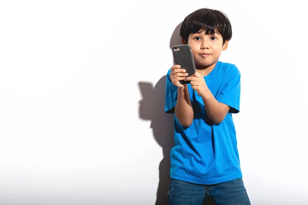 小男孩玩手机游戏肖像白色背景与硬光 穿着蓝色衬衣和琴的混血男孩 愉快的心情 — 图库照片