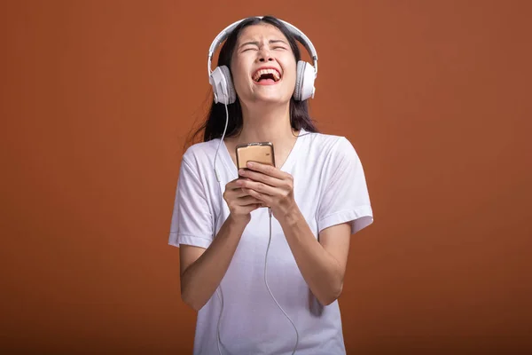 在橙色背景下 通过电话隔离的妇女听音乐 年轻的亚洲女人带着手机听音乐 心情非常愉快 时髦的生活方式概念 — 图库照片