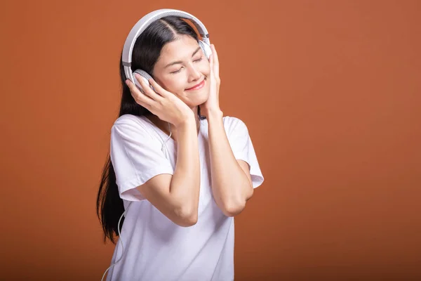 Woman using headphone isolated over orange background. Young asian woman listen to music with head phone, relax happy mood. Hipster lifestyle concept,
