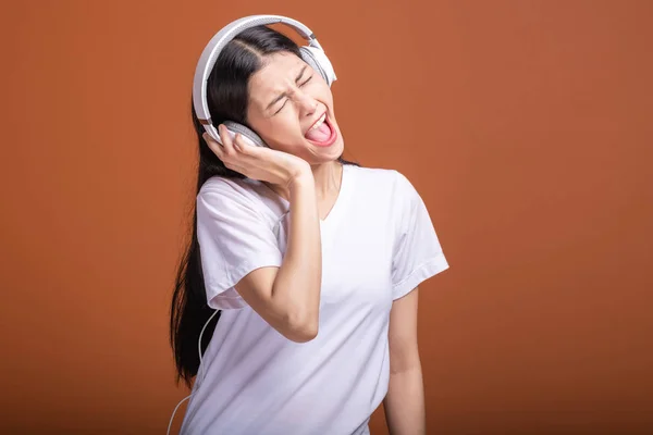 在橙色背景下使用耳机隔离的妇女 年轻的亚洲妇女听音乐与头电话 激动的心情 时髦的生活方式概念 — 图库照片
