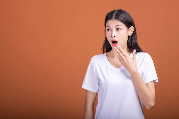 Surprise woman over orange background. Young Asian hipster woman in white t-shirt with surprise pose, hand over mouth. Young woman hipster concept.