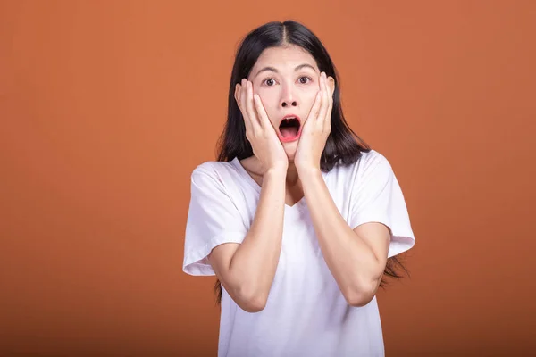 Surprise woman over orange background. Young Asian hipster woman in white t-shirt with very surprise pose, hands cover face. Young woman hipster concept.