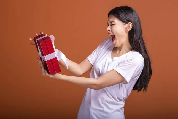 Young hipster girl got a gift. Asian woman in white t-shirt holding a red present gift box, very exciting mood. Holiday gift concept.