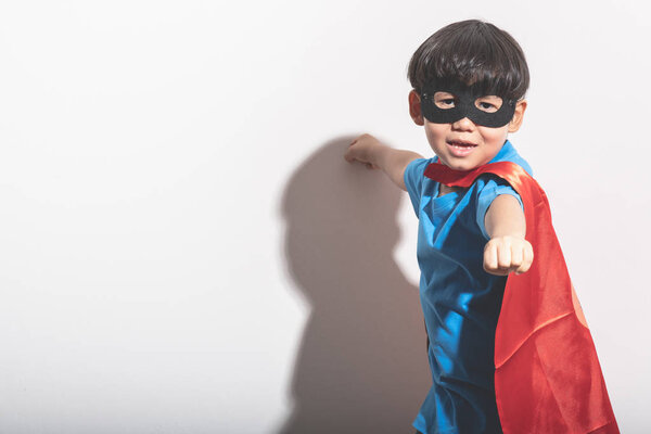 Young boy super hero portrait in white background with hard light. Mixed race boy in blue shirt, jean, mask, cape. Ready to fight pose.