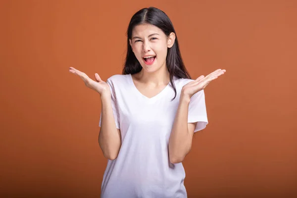 Surprise woman over orange background. Young Asian hipster woman in white t-shirt with happyl surprise pose, open arms. Young woman hipster concept.