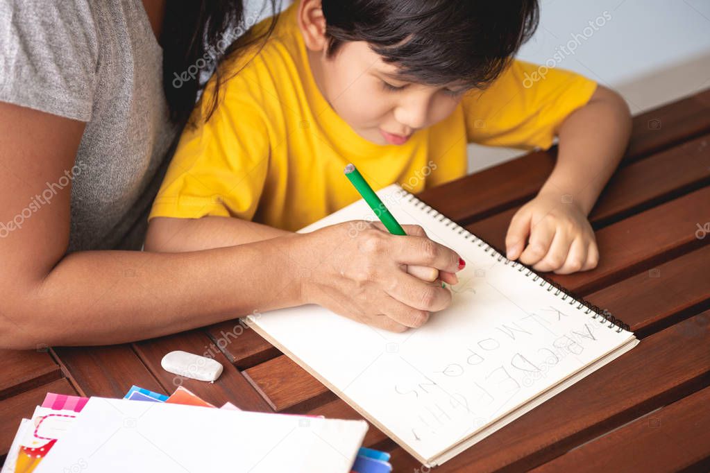Children homework. Young mixed race boy doing homework in terrace at home with his mother teaching him. Writing practice. Focus mood. Back to school concept.