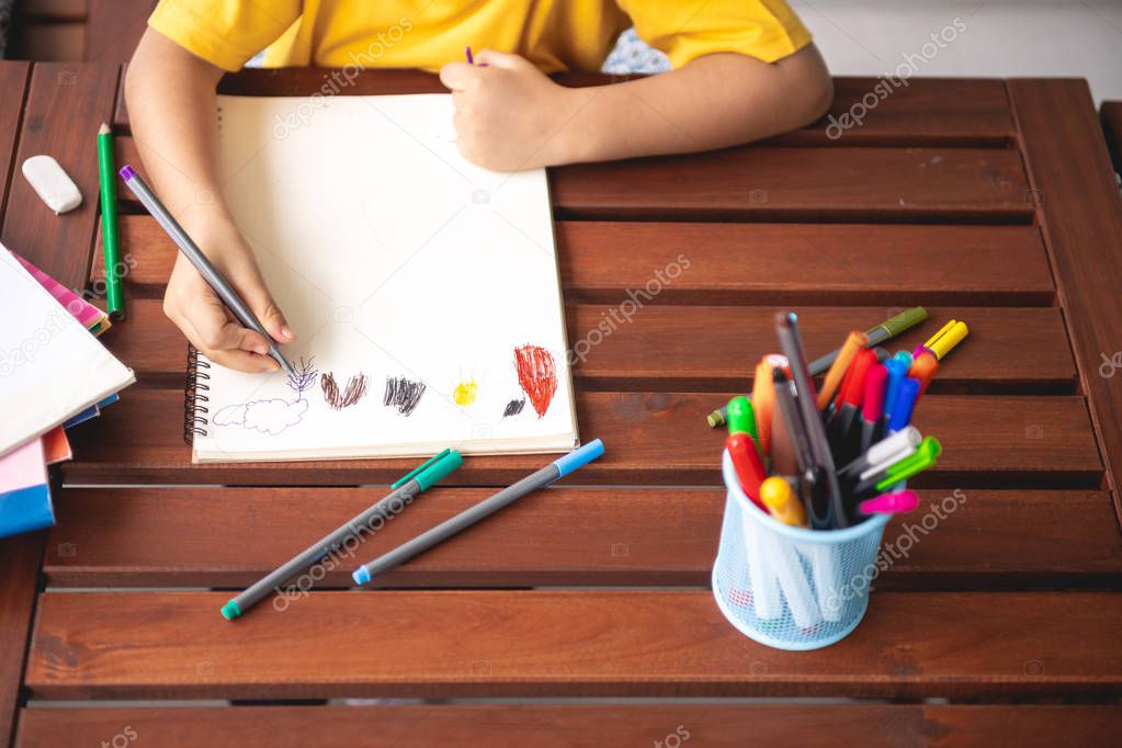 Children homework. Young mixed race boy doing homework in terrace at home. Drawing coloring. Focus mood. Back to school concept.