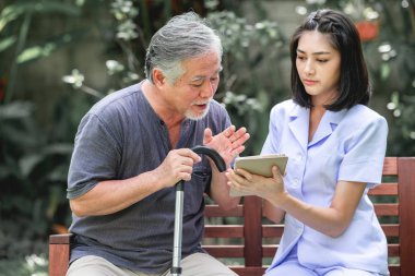 Hemşire hasta birlikte tablet vasıl seyir bankta oturmuş ile. Asyalı yaşlı adam ve birlikte konuşurken oturan bir genç bayan. Ruh sakin ol.