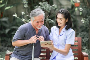 Hemşire hasta birlikte tablet vasıl seyir bankta oturmuş ile. Asyalı yaşlı adam ve birlikte konuşurken oturan bir genç bayan. Ruh sakin ol.