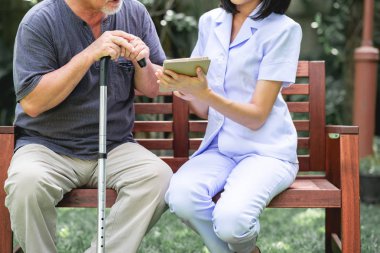 Hemşire hasta birlikte tablet vasıl seyir bankta oturmuş ile. Asyalı yaşlı adam ve birlikte konuşurken oturan bir genç bayan. Ruh sakin ol.