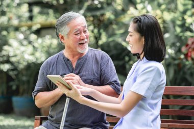 Hemşire hasta birlikte tablet vasıl seyir bankta oturmuş ile. Asyalı yaşlı adam ve birlikte konuşurken oturan bir genç bayan. Ruh sakin ol.