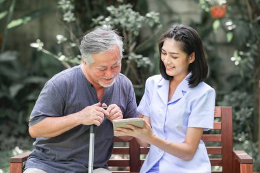 Hemşire hasta birlikte tablet vasıl seyir bankta oturmuş ile. Asyalı yaşlı adam ve birlikte konuşurken oturan bir genç bayan. Ruh sakin ol.