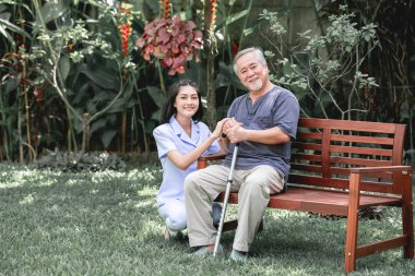 Hemşire ile hasta birlikte konuşurken bankta oturan. Asyalı yaşlı adam ve birlikte konuşurken oturan bir genç bayan. Ruh sakin ol.