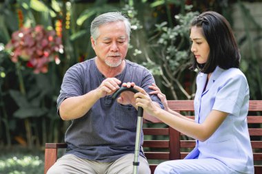Hemşire ile hasta birlikte konuşurken bankta oturan. Asyalı yaşlı adam ve birlikte konuşurken oturan bir genç bayan. Ciddi ruh hali.