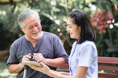 Hemşire hasta birlikte tablet vasıl seyir bankta oturmuş ile. Asyalı yaşlı adam ve birlikte konuşurken oturan bir genç bayan. Ruh sakin ol.